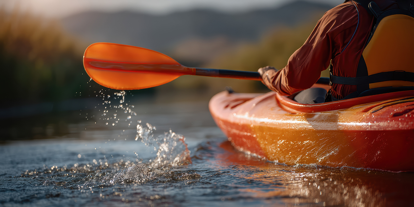 Kayaker with orange paddle on waters edge