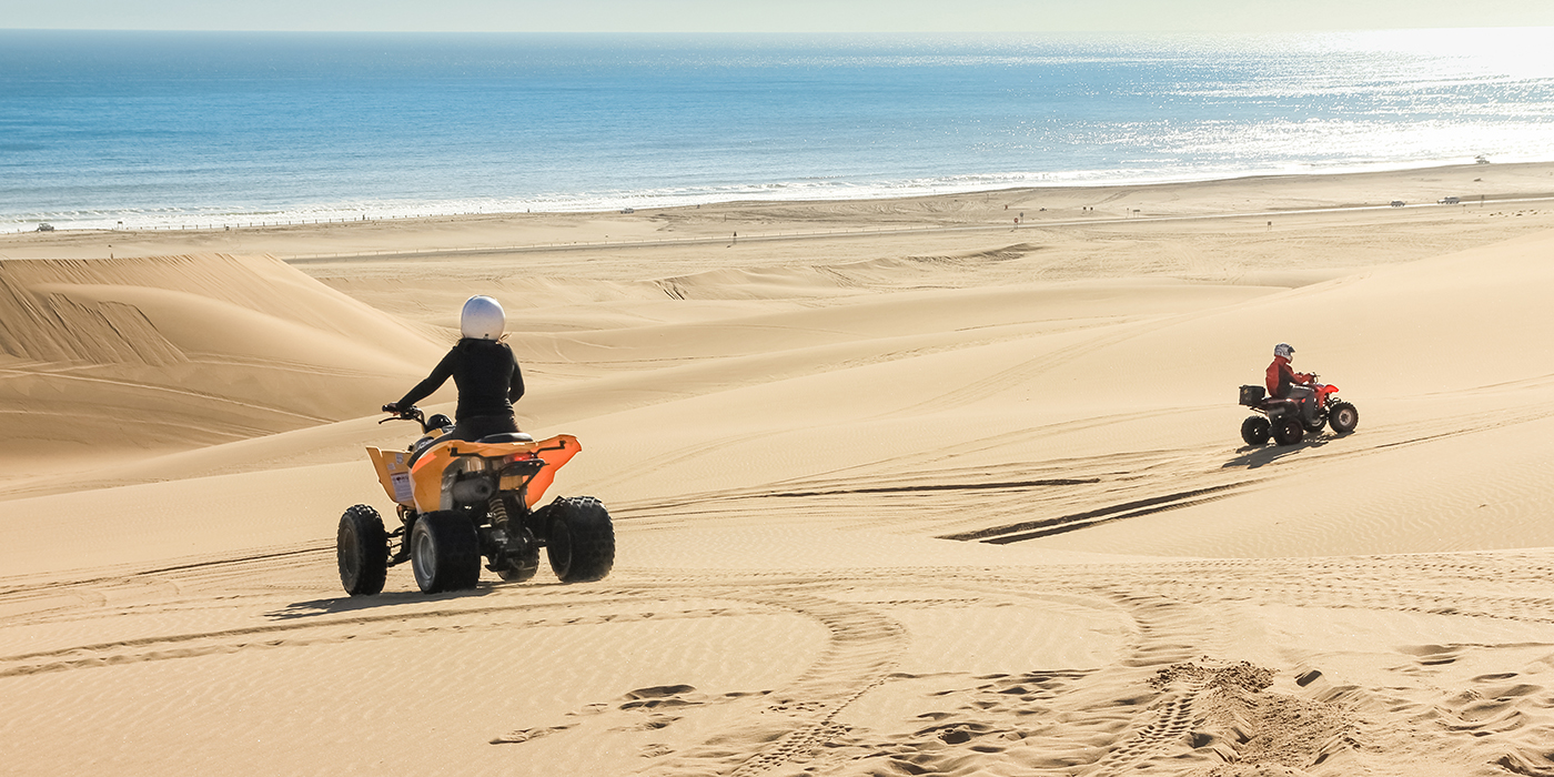 Quad driving people - two happy bikers in sand desert dunes at ocean coast beach, Africa, Namibia, Namib, Walvis Bay, Swakopmund.