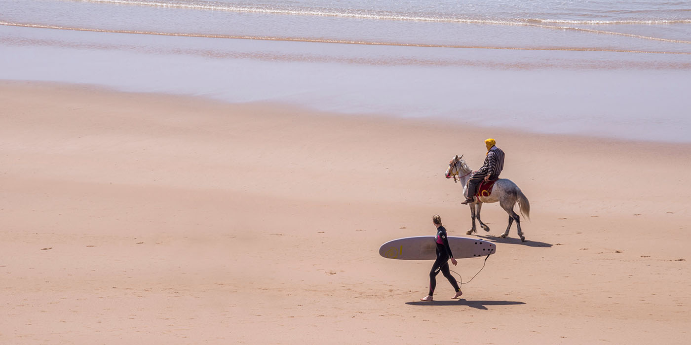 Paisaje con surfista y jinete en la costa de Taghazout en el sur